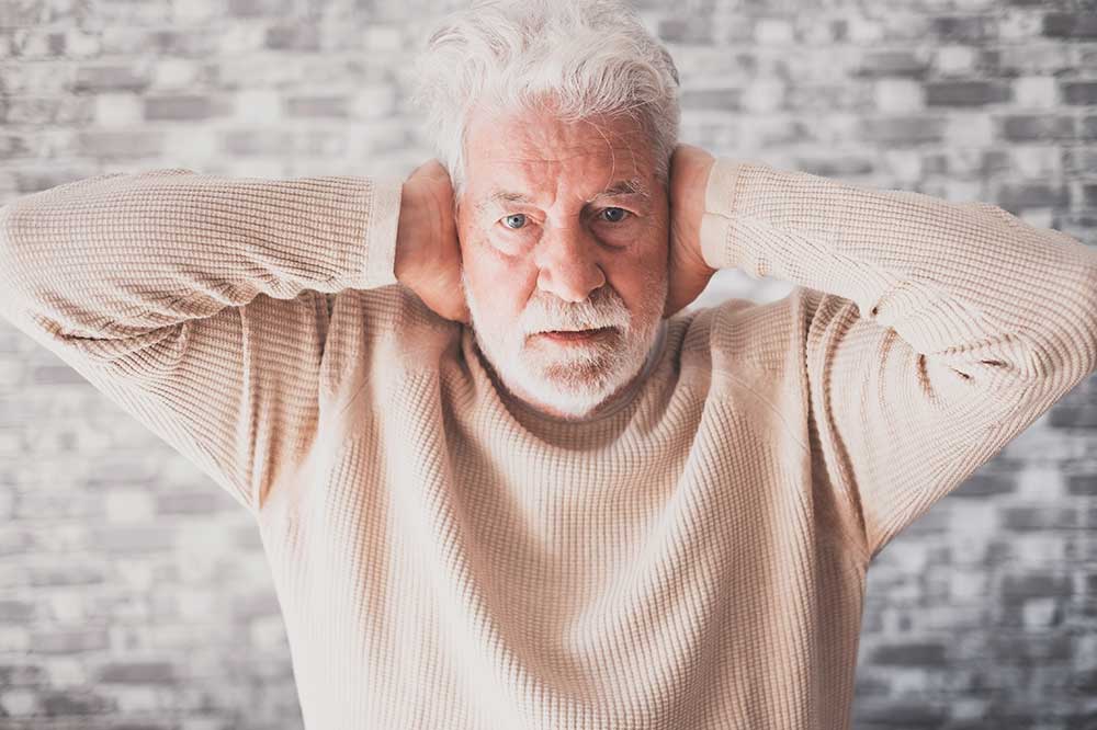 Older man covering both ears over a muffled, clogged ear feeling, a concern Calvert Hearing Care evaluates in Allen, Garland and Flower Mound, TX